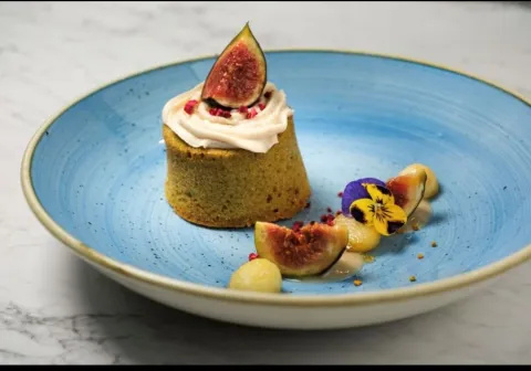 A blue bowl with a fig dessert, topped with creme and fig quarters. Decorated with flower heads.