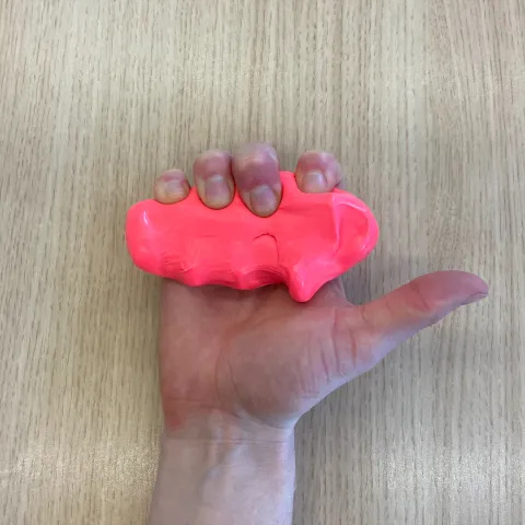 Photo of someone's hands with the ends of the fingers bent into a hook fist position. Their fingers are squeezing some red putty in this position. The thumb is outstretched.