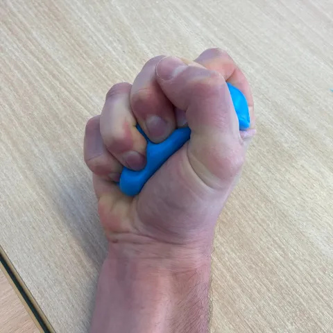 Photo of someone's hand making a ball shape with some blue putty and squeezing it with all of their fingers.