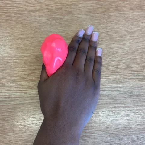 Photo of someone's hand flat on a table. They are squeezing some red putty between their thumb and the side of their hand.