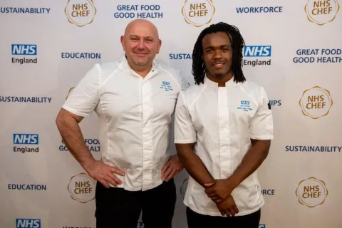 Chef Ned and Chef Joe in chef whites, standing in front of a backdrop with NHS England and other logos