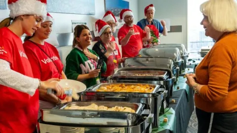 Volunteers serving Christmas meals out of metal chafing dishes to staff. 