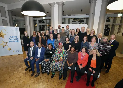 A group of approximately 30 people sitting and standing next to a large banner marked 'Long Service Awards'.