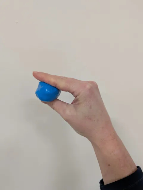 Photo of someone's hand pinching blue putty between their thumb and fingers.