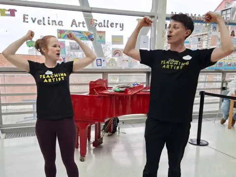 Two Disney teaching artists performing in Evelina London Children's Hospital's atrium, they are in the middle of singing and striking a 'strong man' pose