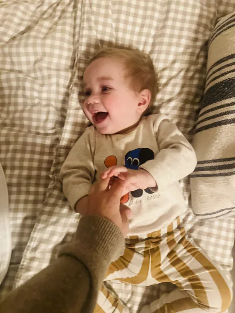 Atlas lying on a bed laughing while a hand is tickling him. 