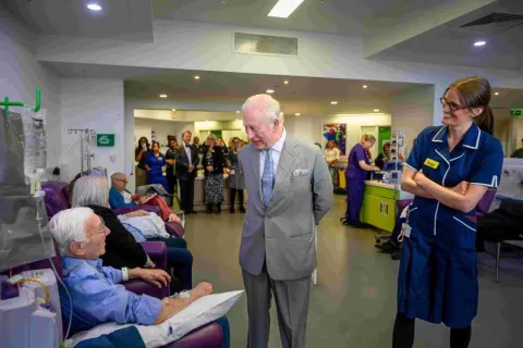 The King meeting a patient who is receiving chemotherapy treatment, whilst a nurse looks on