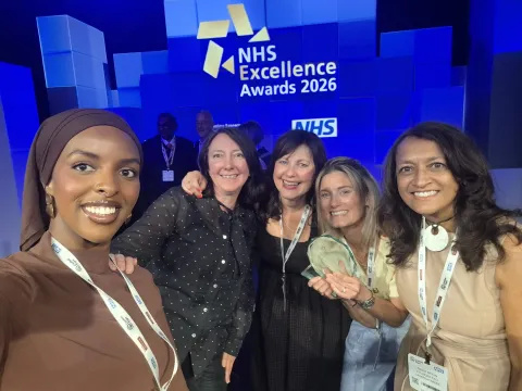 Five people standing in front of an NHS banner. One is holding a glass object.