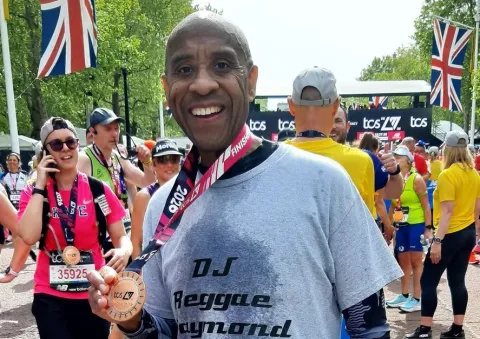 A man stands holding a medal. Behind him are several people and flags.