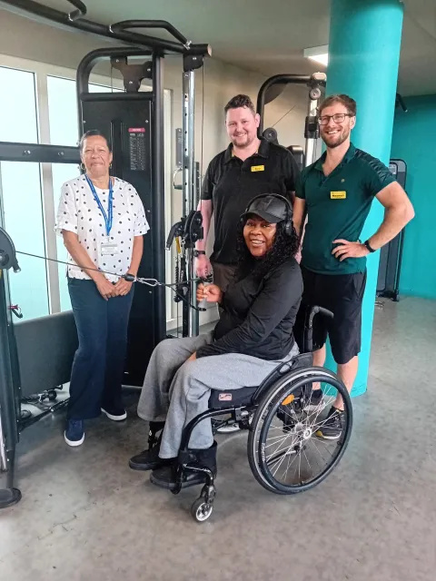 A patient in a wheelchair with physiotherapy staff in a community gym 