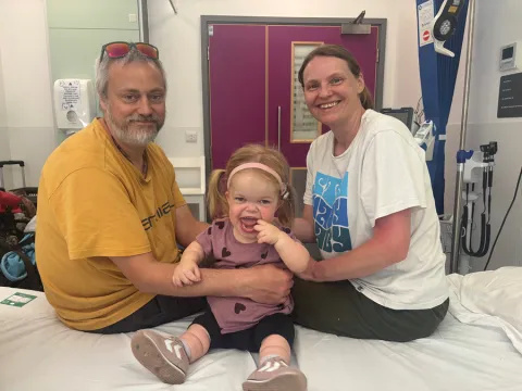 Maisie is sitting on a hospital bed with her parents
