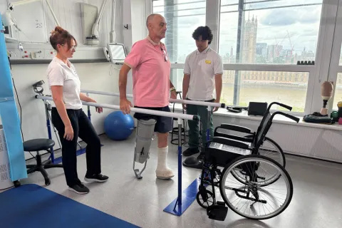 Amputee patient using the bars and supported by two members of staff in the gym