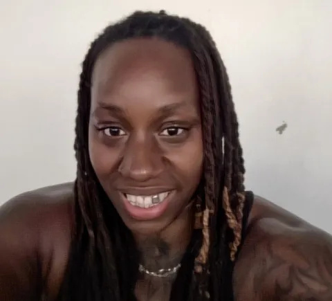 Headshot of Angel, who is wearing a black strappy top. She has long, dark braids.