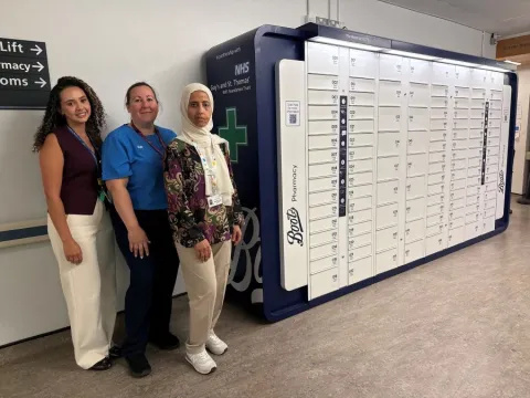 Three pharmacy staff members stand next to the bank of lockers, which have Boots and Guy's and St Thomas' branding on their ends.