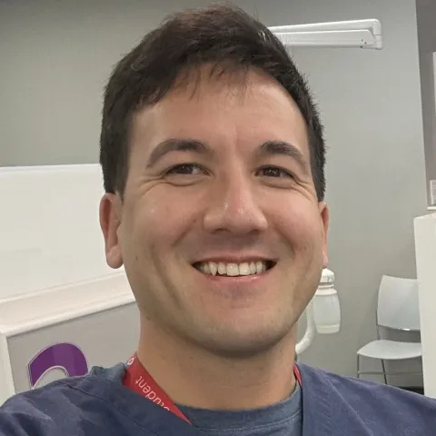 Headshot of Mike Brown, dental technician. He is wearing a blue scrub top and standing in a clinical setting.