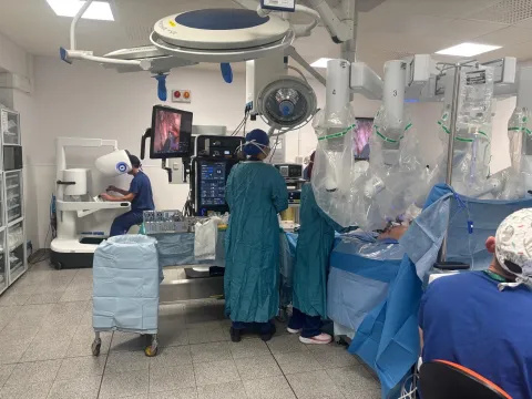 A number of surgical staff are pictured around a patient and the da Vinci 5 robotic-assisted surgical system during a procedure. Professor James Gossage is pictured in the background, sitting at the control console of the robotic system.