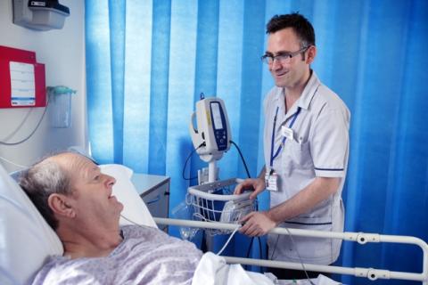 Patient in hospital bed, being talked to by Nursing Assistant