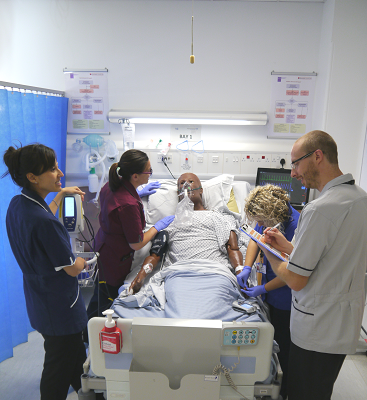 Four people surrounding a mannequin in a hospital bed working on simulated task