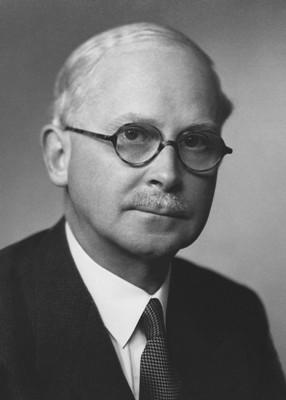 A black and white photograph of Harold Ridley. He is a white man with short white hair and glasses. He is wearing a dark suit